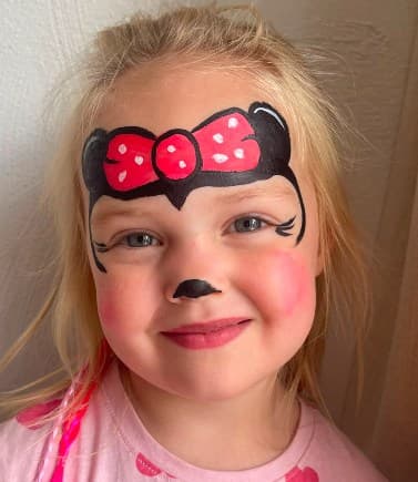 Meisje met Minnie Mouse-schmink: rode strik met stippen, oortjes en roze wangen